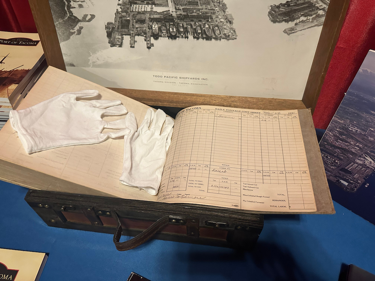 White gloves placed on an old ledger book atop a vintage suitcase.