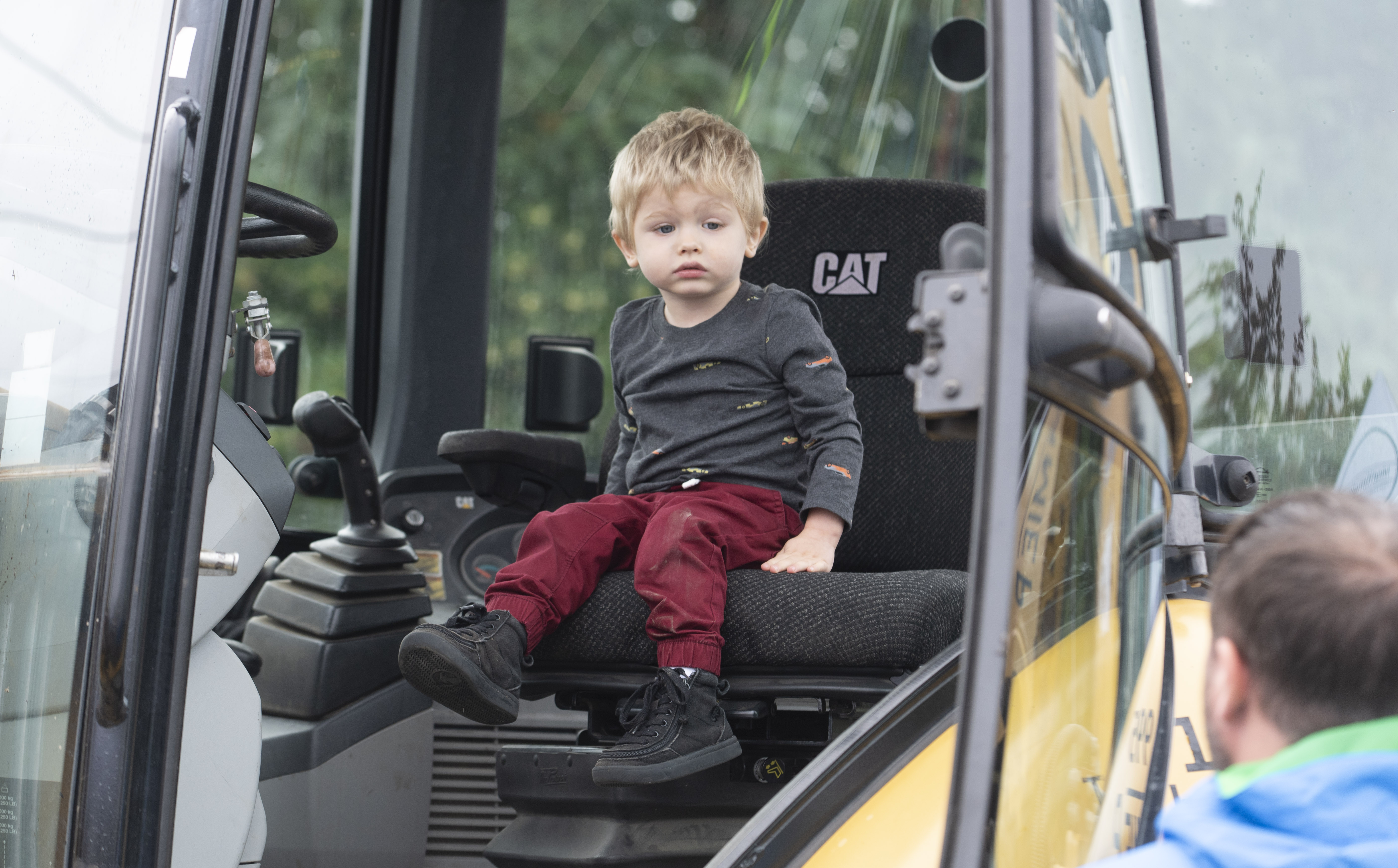 A toddler in red pants sits in a construction vehicle. 