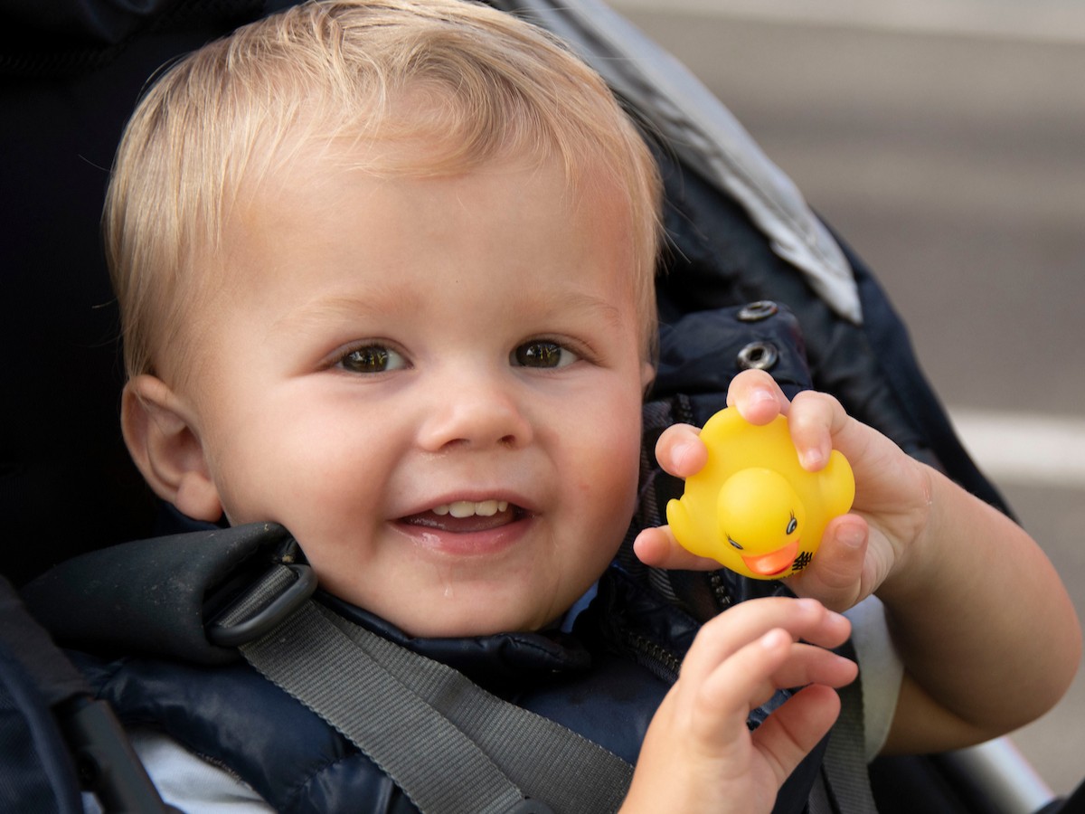 A baby boy holds up a yellow rubber duck to the camera. 
