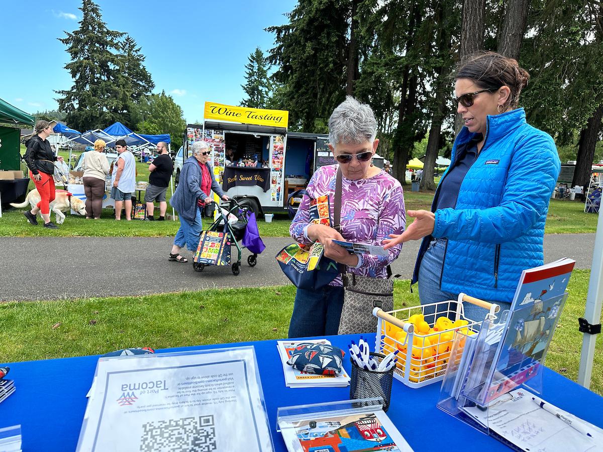 A woman in a blue coat talking to an older woman in a purple shirt at an event booth. 