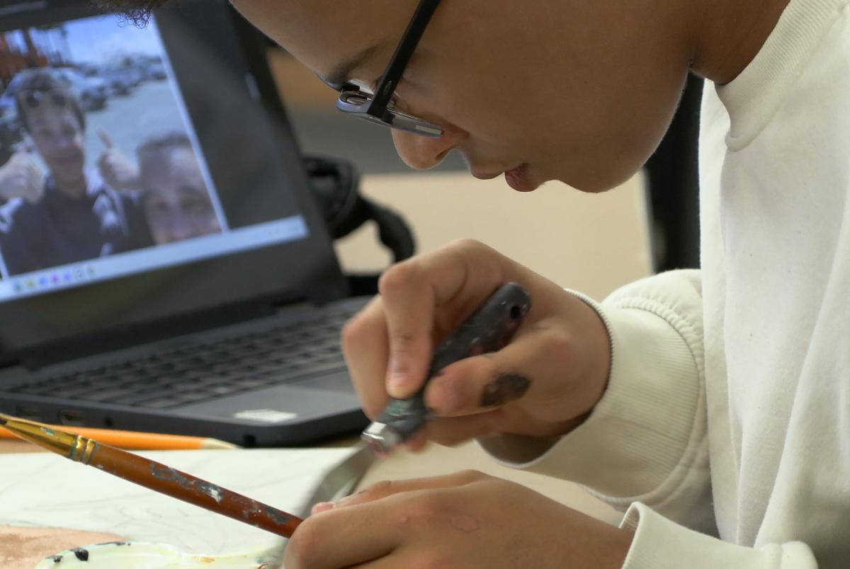 High schooler Xavier King leans close to a portrait he's painting next to his laptop.