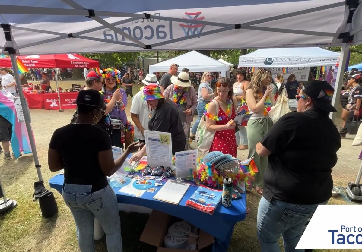 Two Port employees standing behind the Port booth speaking with communit members at Tacoma Pride.