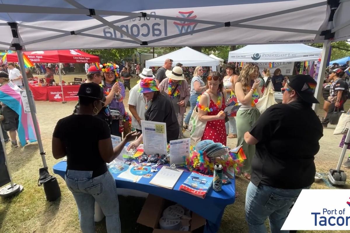 Two Port employees standing behind the Port booth speaking with communit members at Tacoma Pride.
